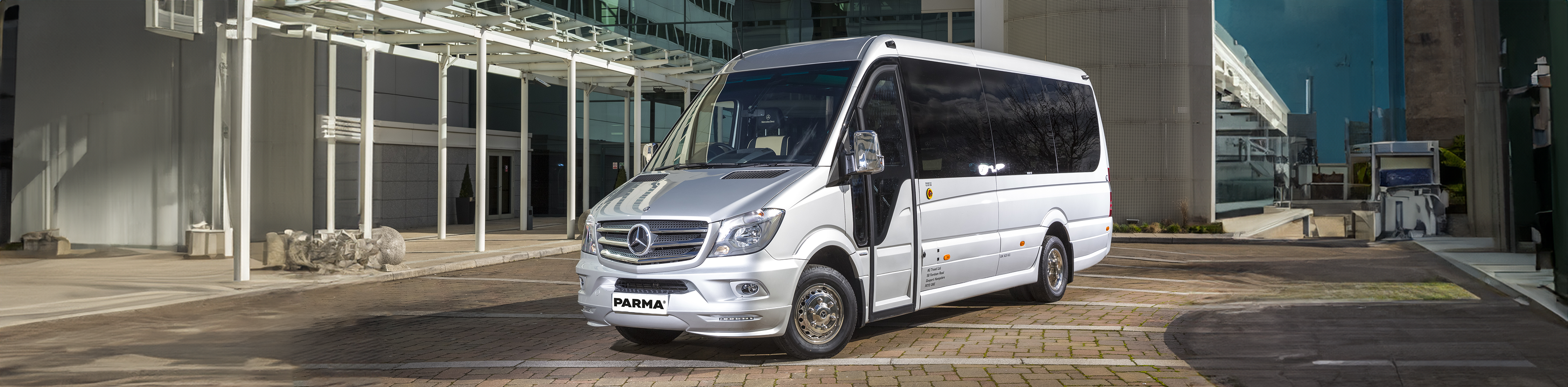 Sleek parma van A silver minibus outside of a commercial office-looking building. It's parked almost head on to us, but we can see the side. The windows are blacked out, and it looks incredibly sleek and modern. the number plate reads 'PARMA'.