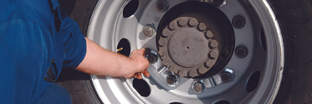 A man is holding a prolock wheel safety nut lock on a large commercial wheel. He's in a blue boiler suit.