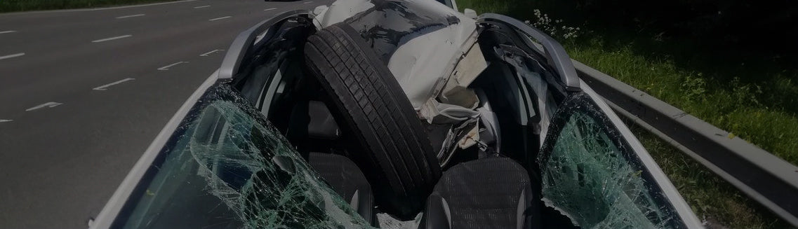 HGV Wheel in Car A faded banner image of a car with an HGV wheel through the front windscreen. The front of the car is significantly crushed and caved in.