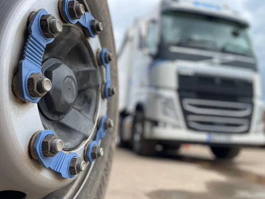 A close up shot of a commercial wheel with blue zafety lug locks attached. behind this wheel you can see a white lorry with matching blue features.