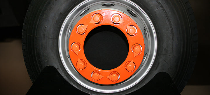 Orange nut ring attached to a HGV wheel. The pop of colour is evident against the black and grey of the rest of the wheel. The holes of the nut ring have the wheel nuts poking through, but these aren't visible because the user has also opted for orange  wheel nut indicators, sticking to the orange branding.