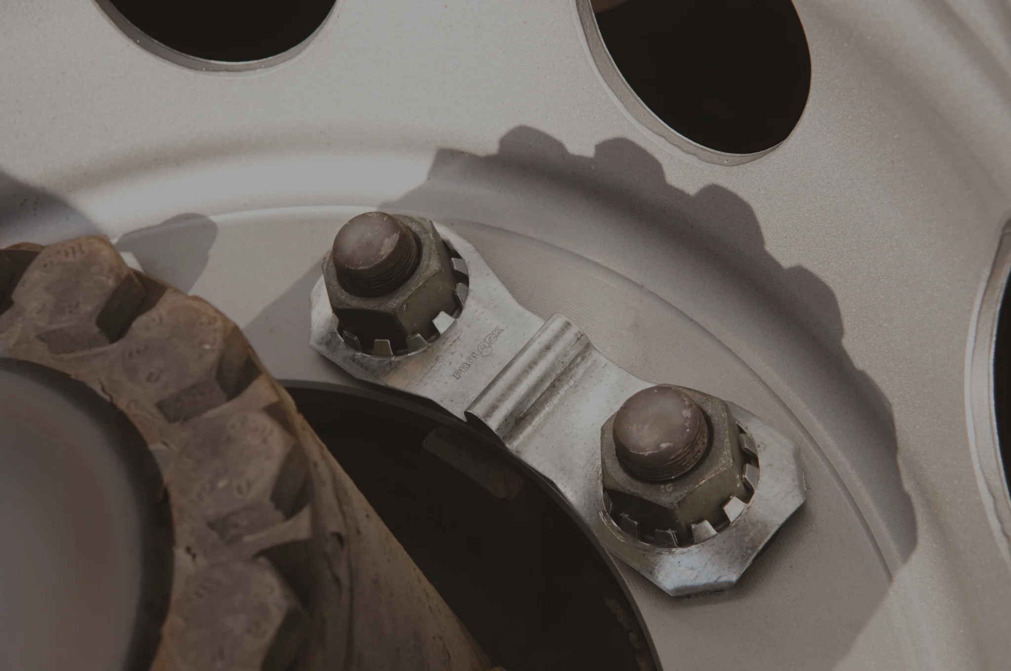 Banner image of a close up shot of a prolock attached to a wheel via the wheel nuts. The image is slightly greyed out to allow the white text to pop over top of it.