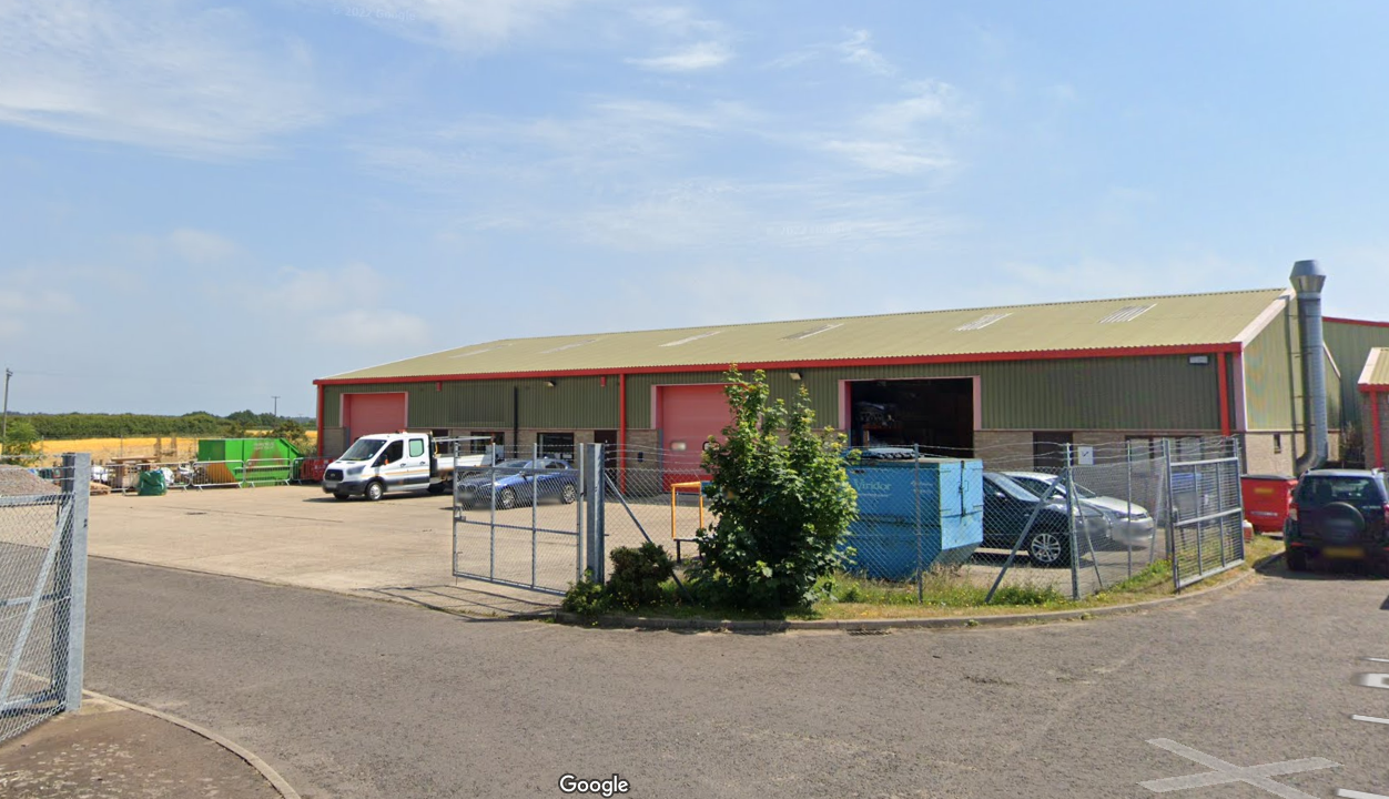 An image of a warehouse, taken from a road. The sky is blue and bright. The warehouse isn't huge but a good size for a first warehouse.