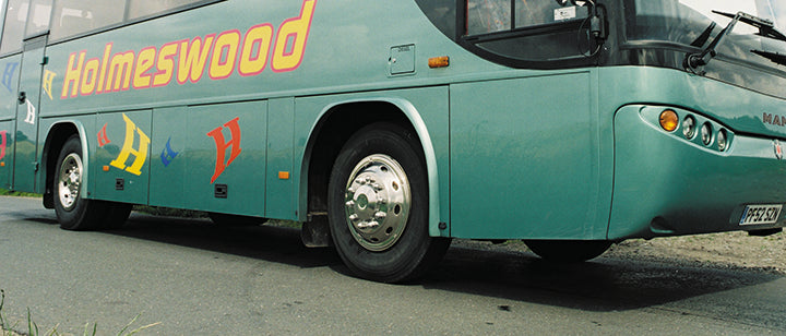 Shows the deluxe style wheel trim on a  green coach. The trim is fitted to the wheel, with the image taken from a low angle. The front wheel is mostly visible, looking shiny and sleek. The back is slightly visible, showing a matching pair.