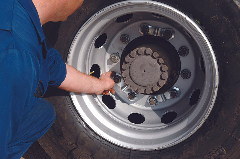 A man is holding a prolock wheel safety nut lock on a large commercial wheel. He's in a blue boiler suit.