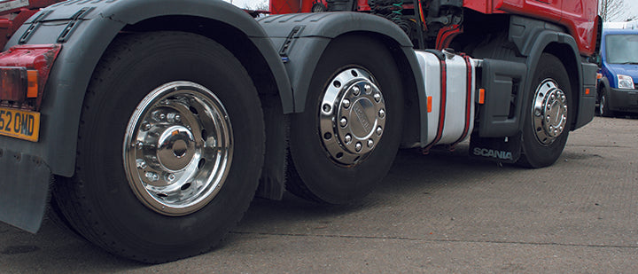 A photo of the bottom portion of a red lorry, taken from slightly behind the vehicle to show all three wheels that hold the cab. The wheel closest to the viewer has the super deluxe trim, showing the depth and sleek design.